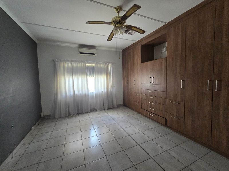 A spacious bedroom featuring extensive built-in wooden cabinetry, tiled flooring, a ceiling fan, and a wall-mounted air conditioning unit.