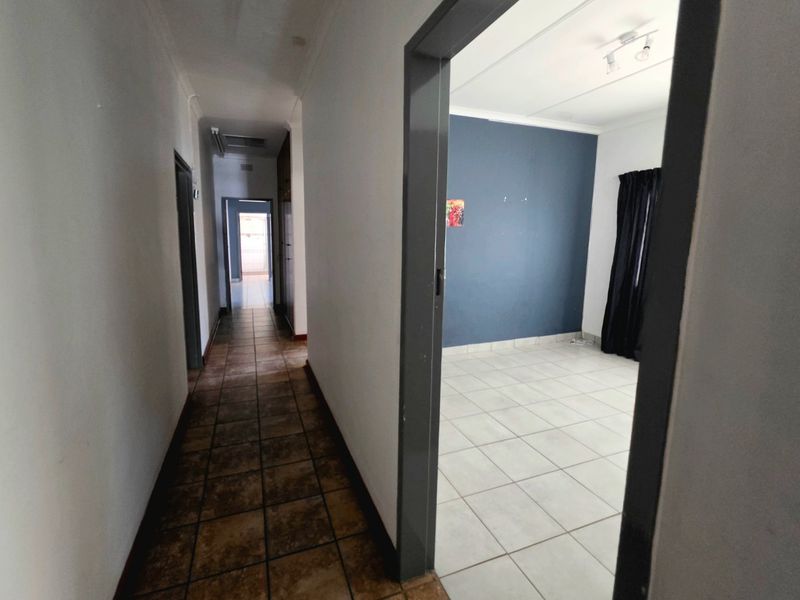A view from a tiled hallway looking into an empty bedroom with white and blue walls and tiled flooring.