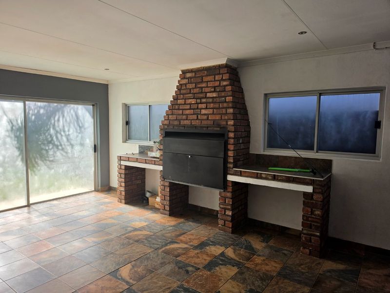 Covered patio area featuring a built-in brick braai, tiled flooring, and sliding glass doors providing access to the outdoor space.