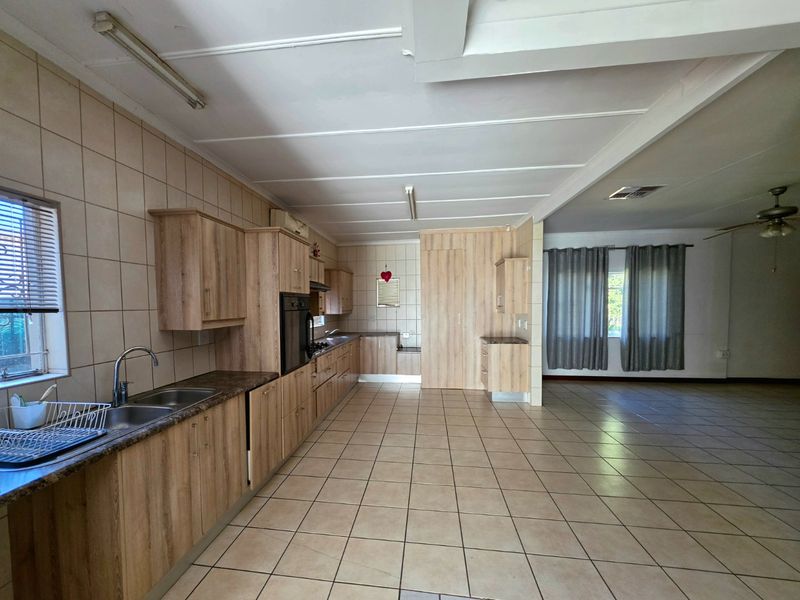 Spacious open-plan kitchen and living area featuring laminate cabinetry, tiled flooring, and built-in oven, offering a functional layout ready for modern updates.