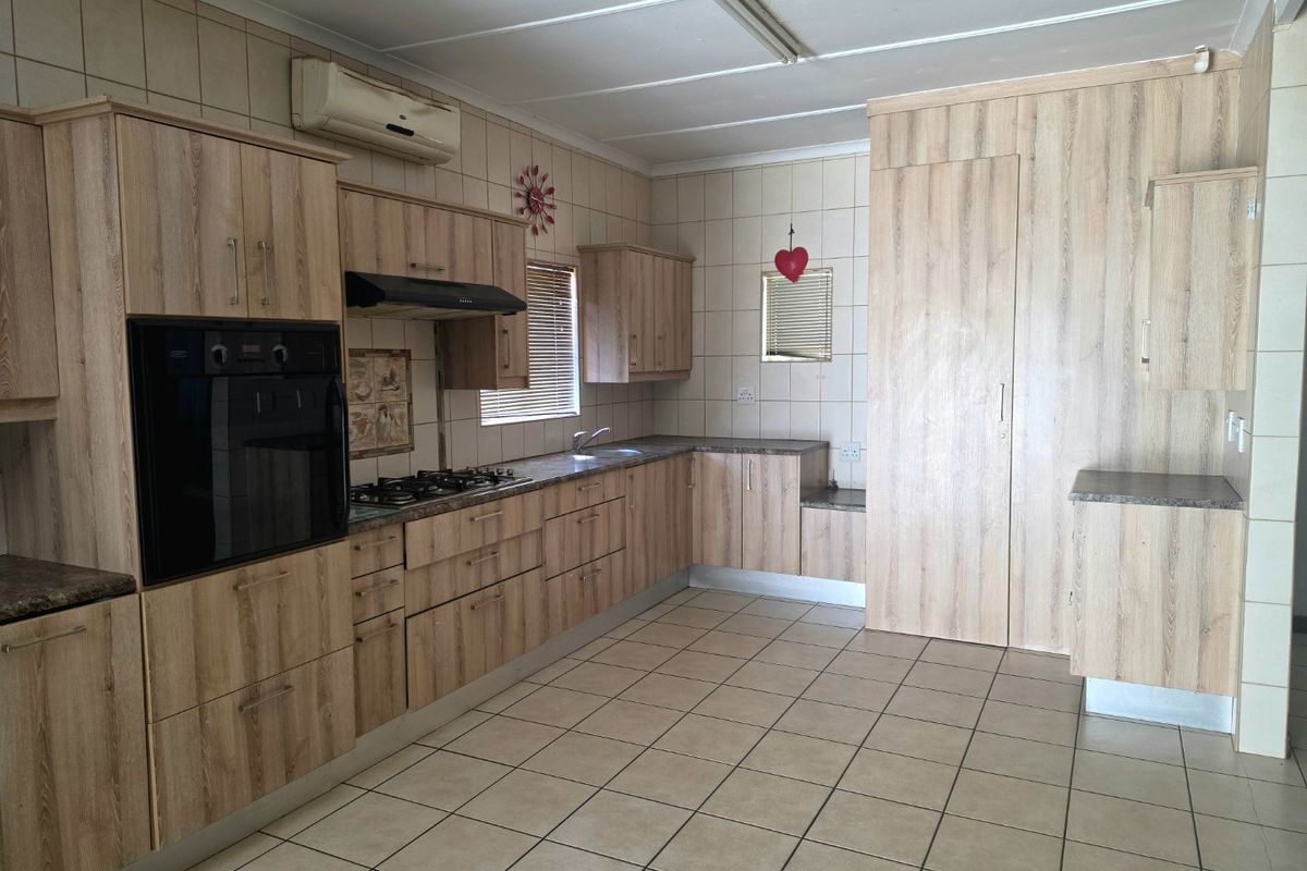 A functional kitchen featuring light wood-look cabinetry, built-in oven and hob, tiled flooring, and wall-mounted air conditioning unit.