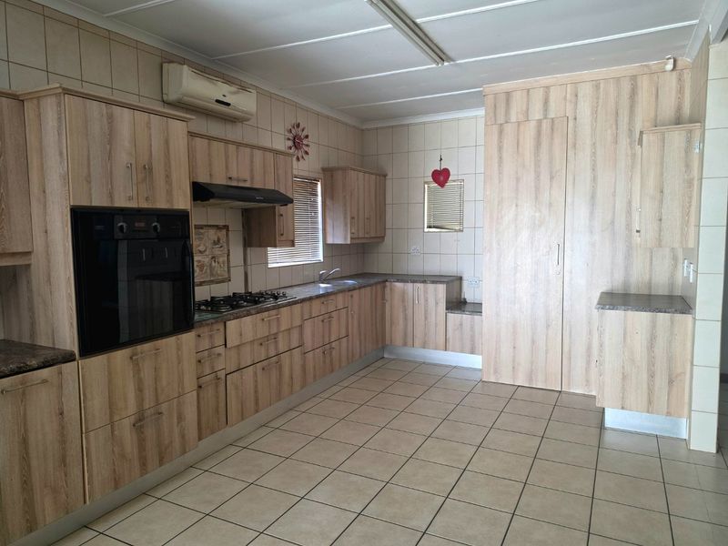 A functional kitchen featuring light wood-look cabinetry, built-in oven and hob, tiled flooring, and wall-mounted air conditioning unit.