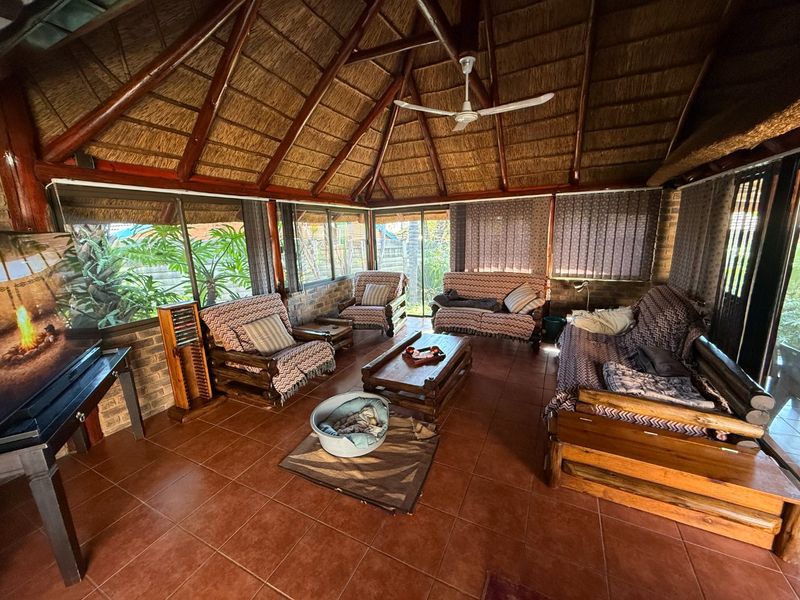 A spacious covered patio featuring a traditional thatched roof with exposed timber rafters, tiled flooring, and large sliding glass doors overlooking the garden.