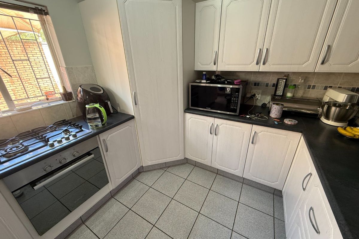 A functional kitchen featuring white cabinetry, dark laminate countertops, a built-in oven with gas hob, and tiled flooring.