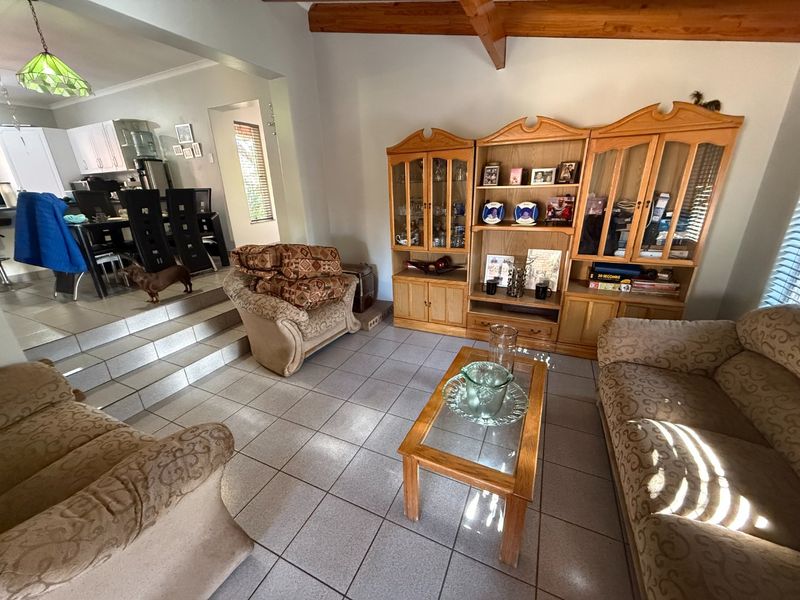 Open-plan living area featuring tiled floors, exposed timber ceiling beams, and a split-level transition leading to an adjacent kitchen space.