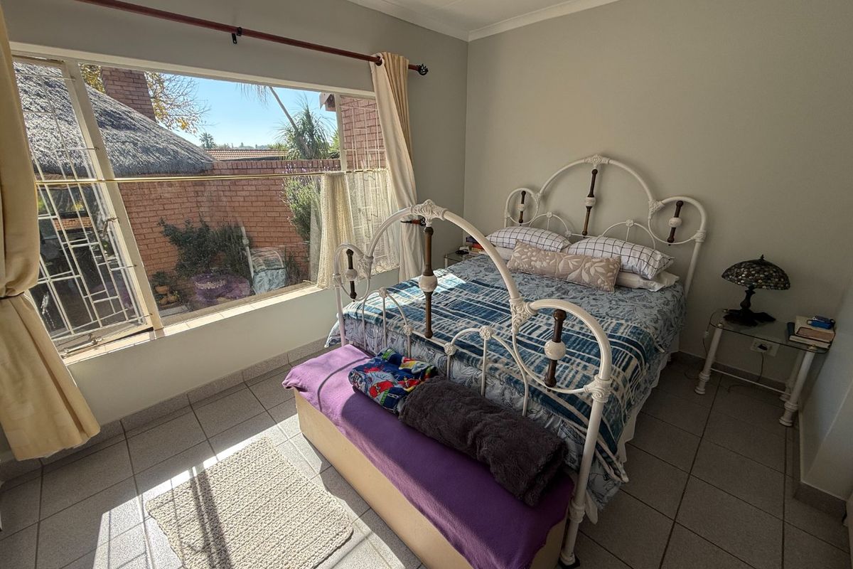 A bedroom featuring large windows that provide natural light and views of the exterior, finished with neutral wall paint and tiled flooring.