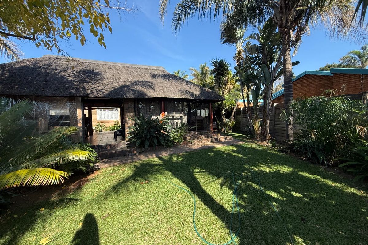 Rear view of the property featuring a thatched roof patio, established garden, and paved walkway, providing a private outdoor living space.