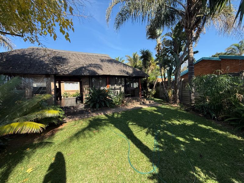 Rear view of the property featuring a thatched roof patio, established garden, and paved walkway, providing a private outdoor living space.