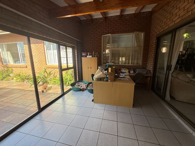 Enclosed patio area featuring exposed timber beams, facebrick walls, and large aluminium sliding doors providing access to the garden.