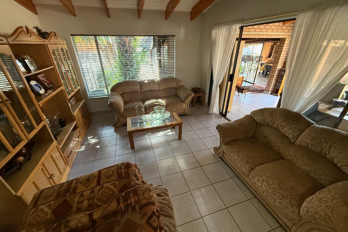 A living room featuring exposed timber ceiling beams, ceramic floor tiles, and a sliding glass door providing access to an outdoor patio area.