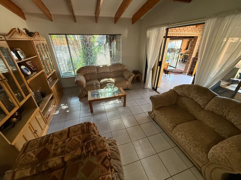 A living room featuring exposed timber ceiling beams, ceramic floor tiles, and a sliding glass door providing access to an outdoor patio area.