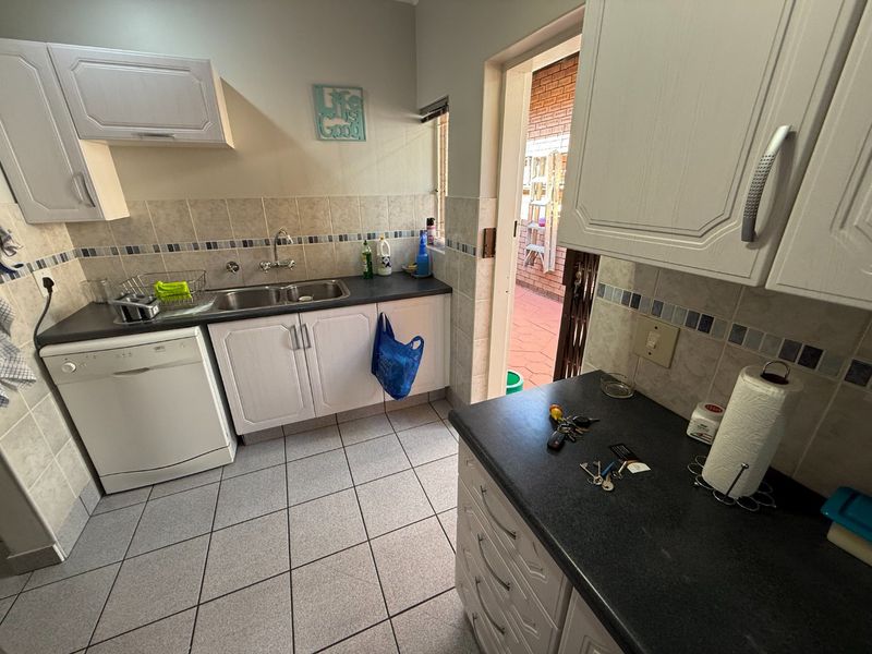 A functional scullery area featuring built-in cabinetry, double basin sink, tiled splashback, and direct access to an outdoor patio area.