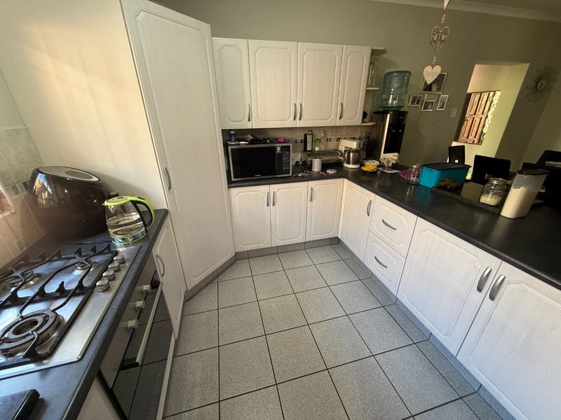 A functional kitchen featuring white cabinetry, dark countertops, a gas hob, and tiled flooring, offering a practical layout for daily meal preparation.