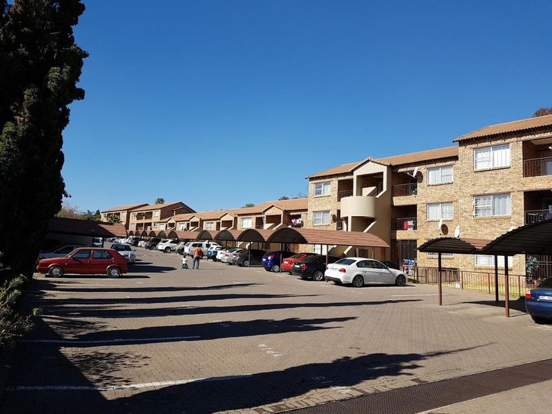 Exterior view of a multi-story residential complex featuring brick facades, tiled roofs, and covered parking bays for residents.