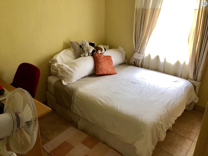 A compact bedroom featuring tiled flooring and natural light from a window with installed curtain rails.