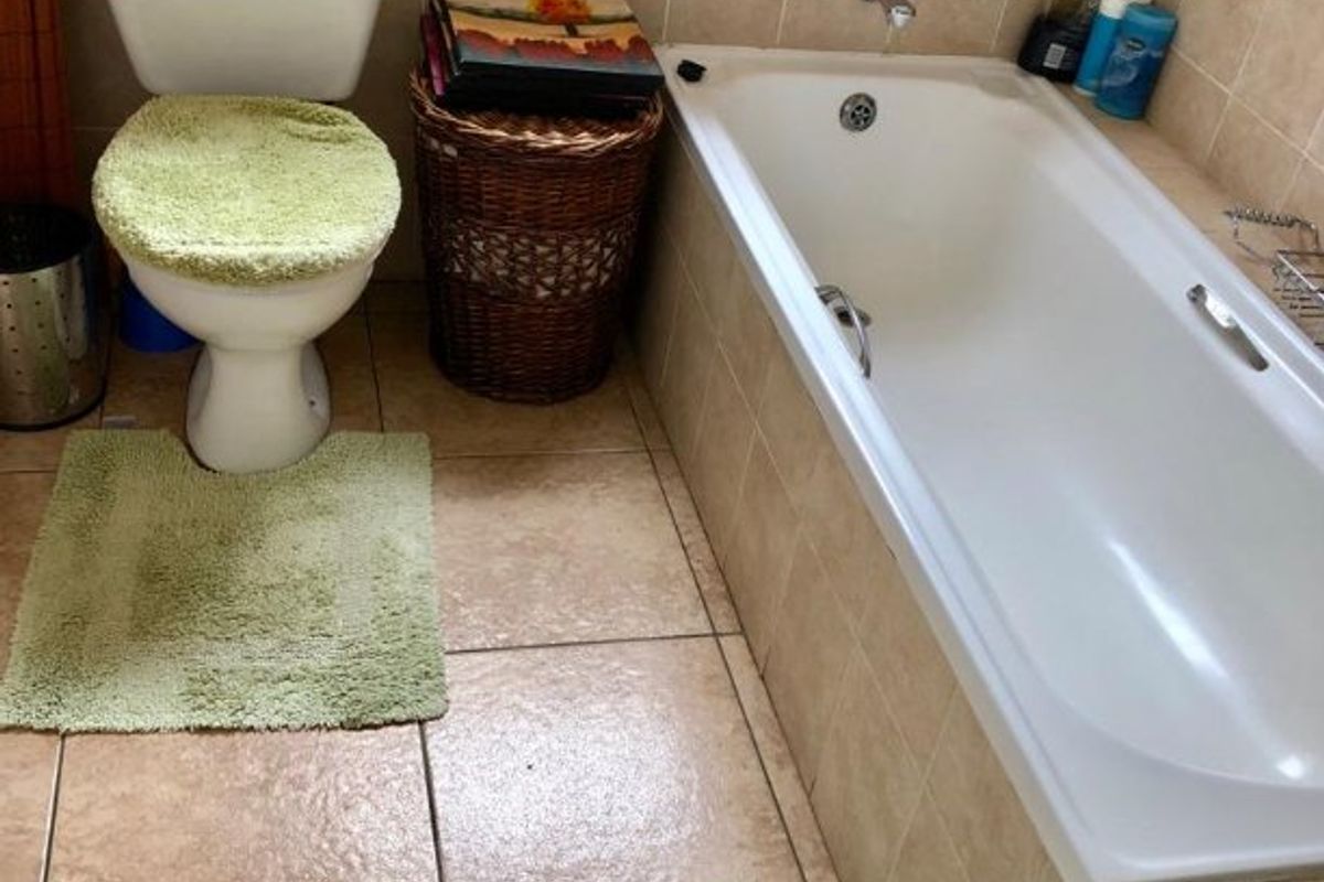 A functional bathroom featuring ceramic floor and wall tiles, a built-in bathtub, and a standard toilet.