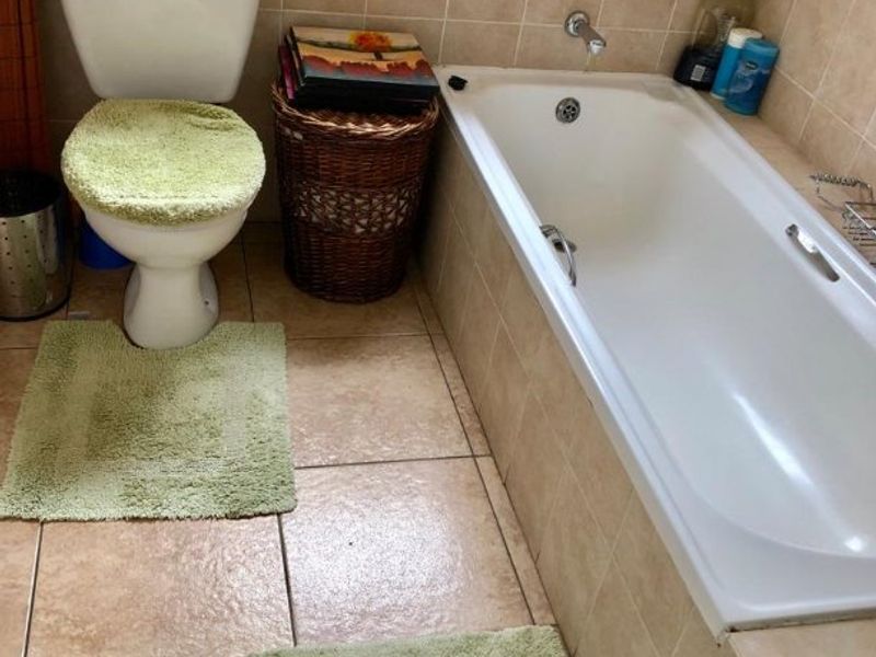 A functional bathroom featuring ceramic floor and wall tiles, a built-in bathtub, and a standard toilet.