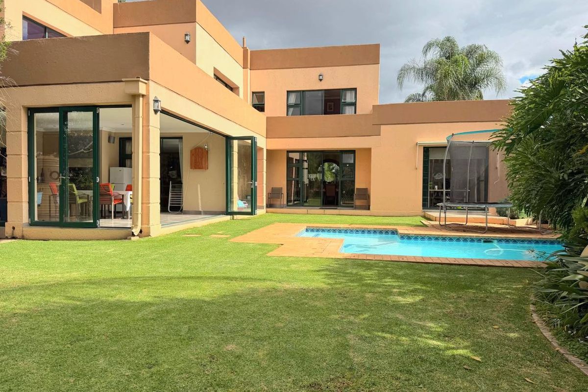 Rear view of the property featuring a well-maintained lawn, swimming pool with paved surround, and large bi-fold doors leading into the home.