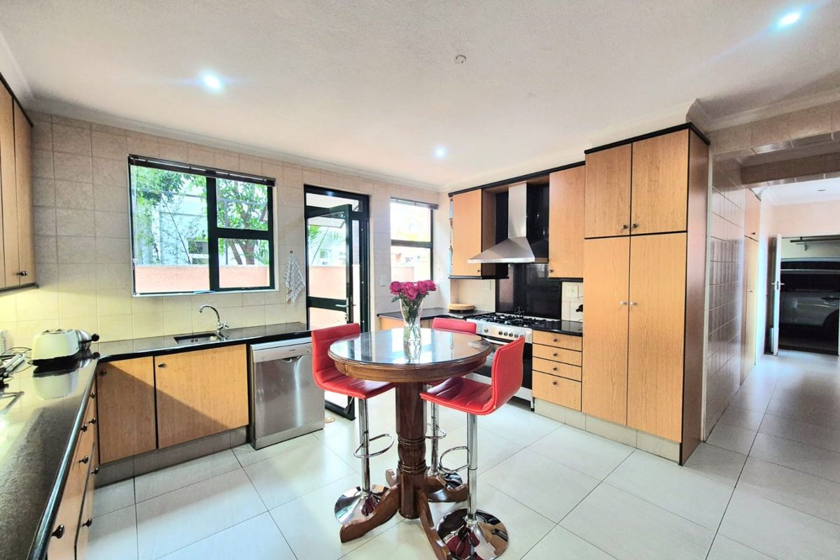 A functional kitchen featuring light wood cabinetry, dark countertops, tiled flooring, and integrated appliances, offering a practical layout with direct outdoor access.