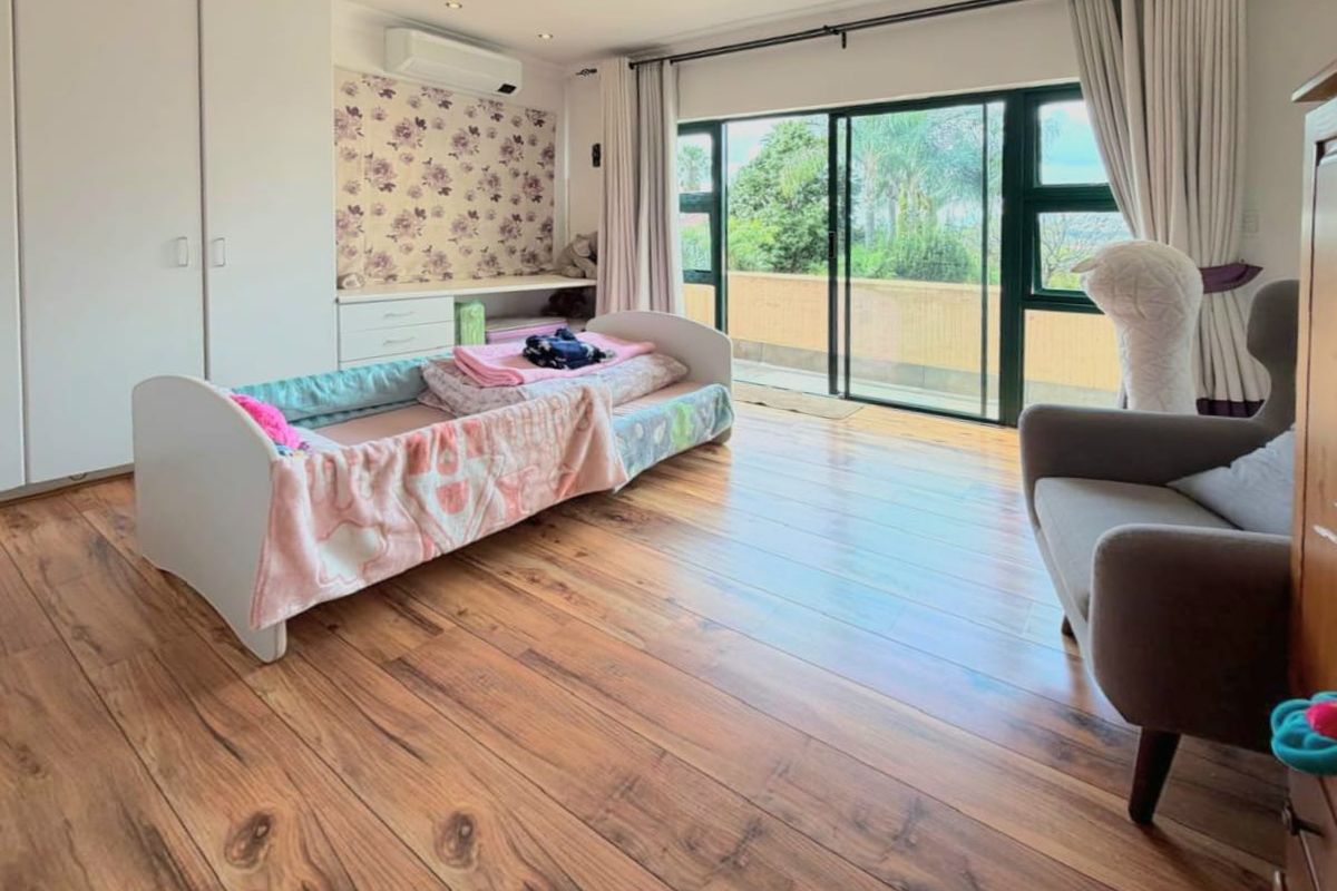 Spacious bedroom featuring laminate flooring, built-in cupboards, a split-system air conditioner, and large sliding glass doors opening to an outdoor balcony.