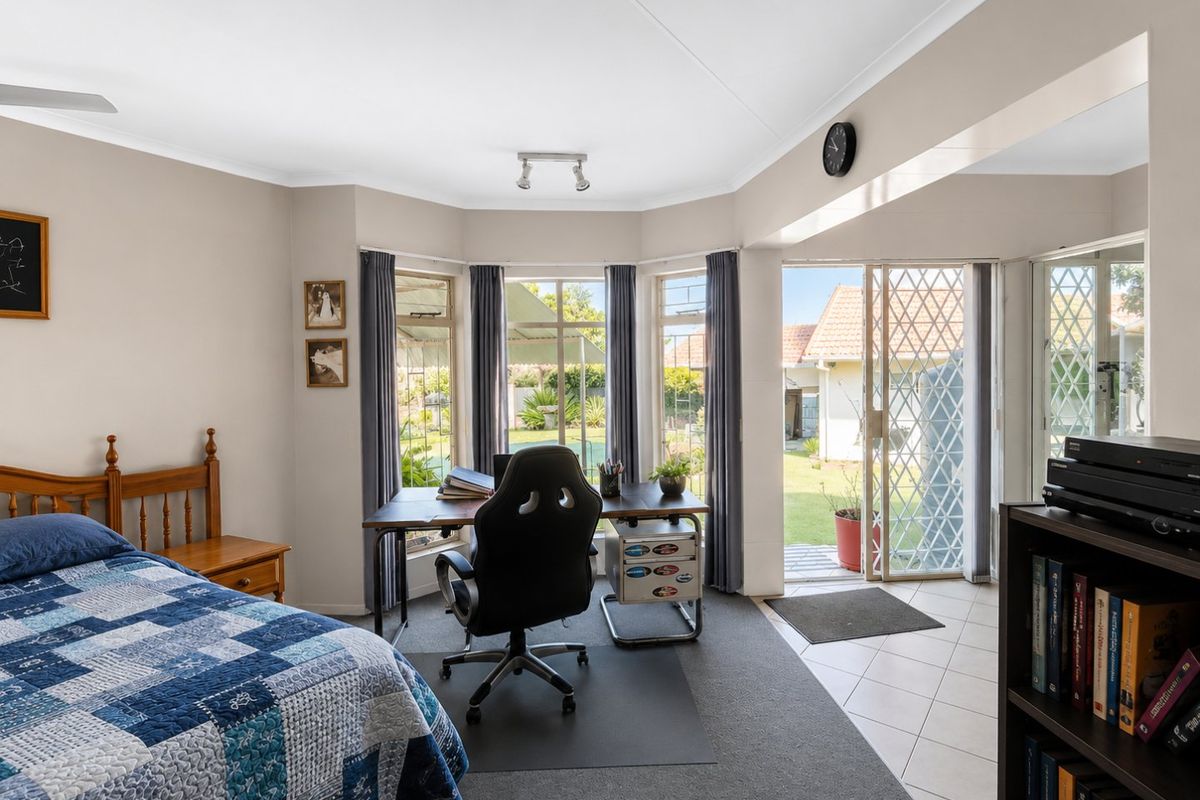 Spacious bedroom featuring a bay window, ceiling fan, and direct access to the garden through a sliding security door.