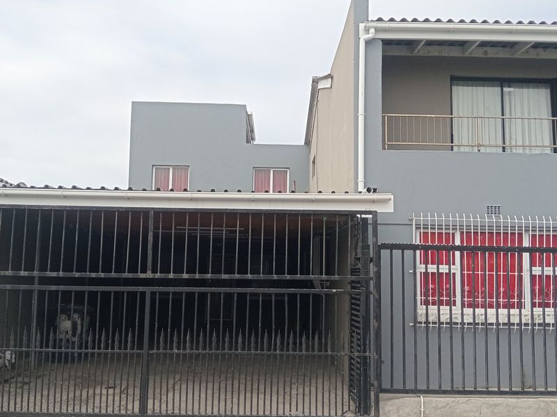 Front exterior view of a two-story house featuring a carport, metal security gates, and an upper-level balcony with sliding doors.