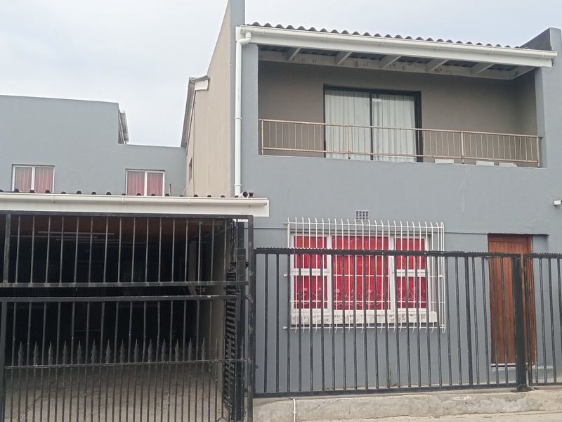 Front elevation of a two-story house featuring a gated carport, ground floor security bars, and an upper-level balcony with a metal balustrade.