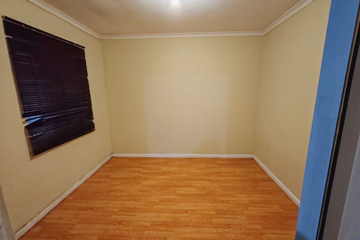An empty bedroom featuring laminate flooring, coving, and a window with fitted blinds.