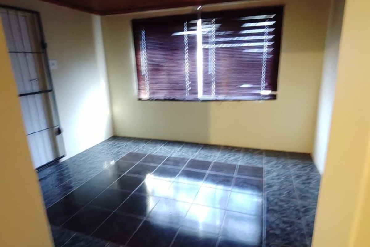 An empty living room featuring dark tiled flooring, a timber-paneled ceiling, and a security gate at the entrance.