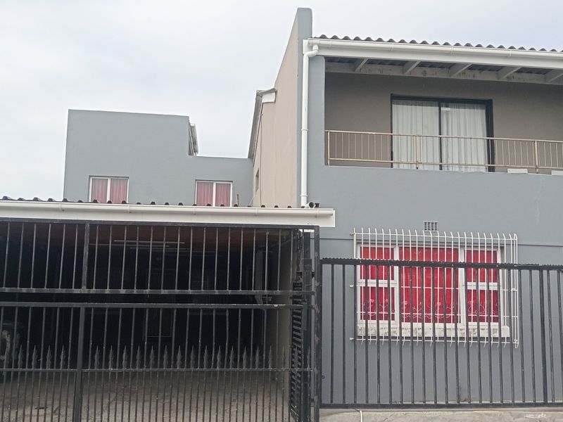 Front elevation of a two-story house featuring a carport, balcony, and secure metal gate access.