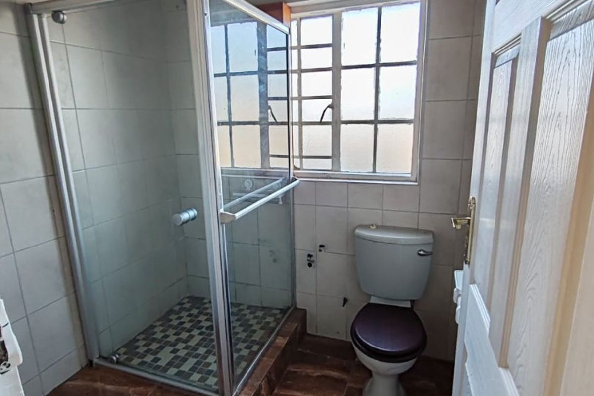 A compact bathroom featuring a shower enclosure, toilet, tiled finishes, and a timber ceiling. The space is currently missing a vanity or basin.