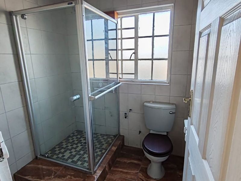 A compact bathroom featuring a shower enclosure, toilet, tiled finishes, and a timber ceiling. The space is currently missing a vanity or basin.