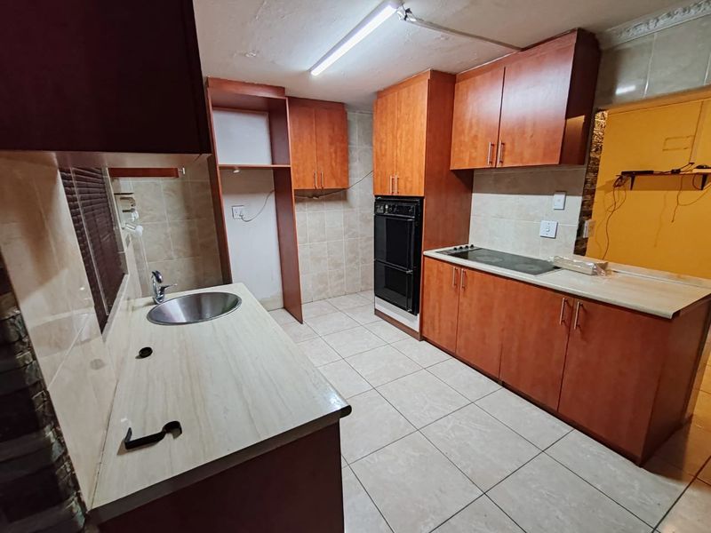 A functional kitchen featuring built-in wooden cabinetry, laminate countertops, a stainless steel sink, and integrated oven and hob with tiled flooring and backsplash.