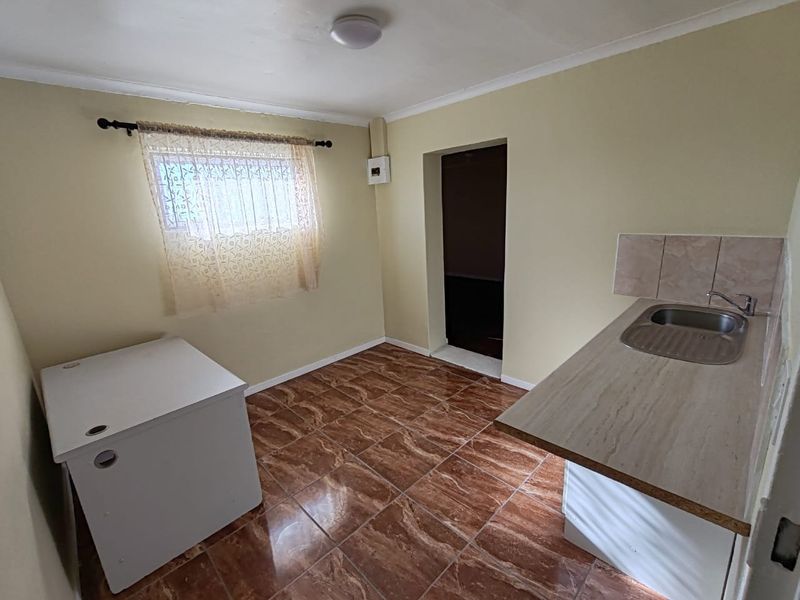 A functional kitchen area featuring tiled flooring, a laminate countertop with an integrated stainless steel sink, and a tiled splashback.