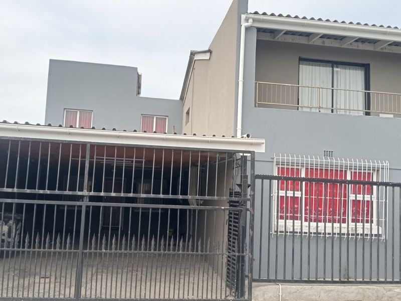 Front elevation of a two-story house featuring a carport, upper-level balcony, and secure metal fencing.