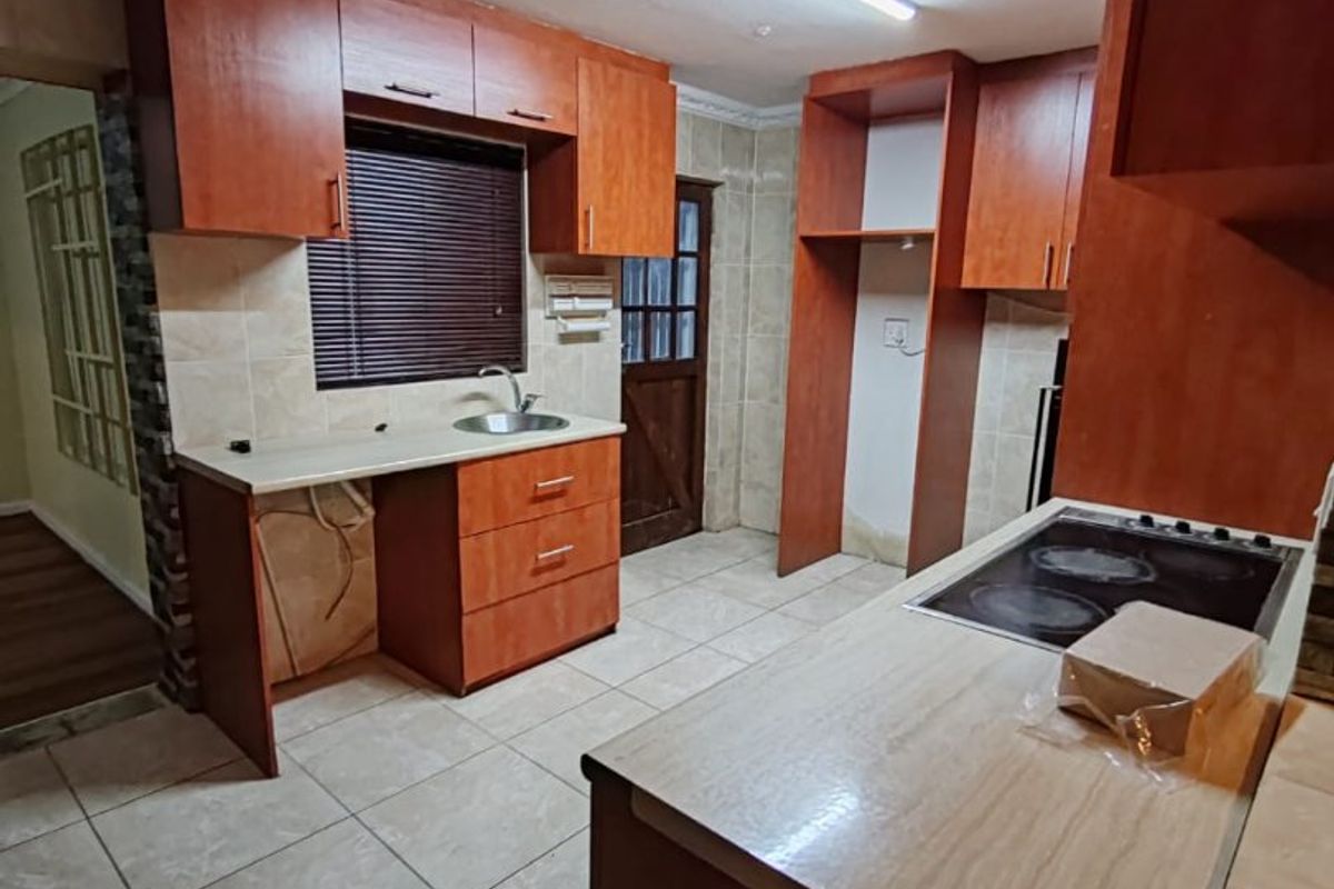 A dated kitchen featuring wood-finish cabinetry, laminate countertops, an integrated electric hob, and ceramic floor tiles, currently vacant and ready for renovation.