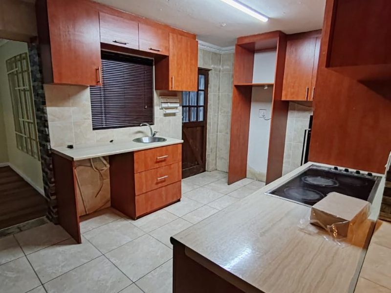 A dated kitchen featuring wood-finish cabinetry, laminate countertops, an integrated electric hob, and ceramic floor tiles, currently vacant and ready for renovation.