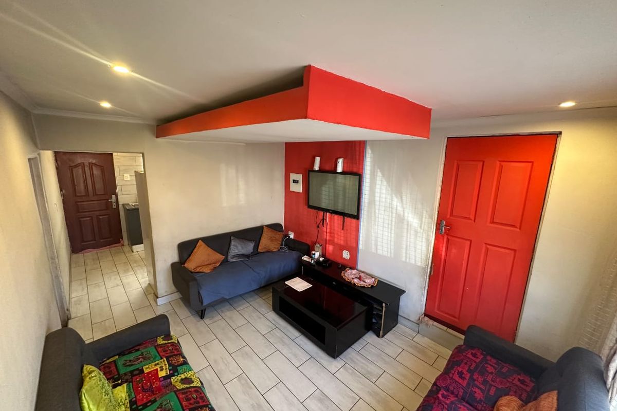 Living room featuring tiled flooring and a distinctive red-painted ceiling bulkhead and accent wall, providing a functional space with direct access to adjacent rooms.