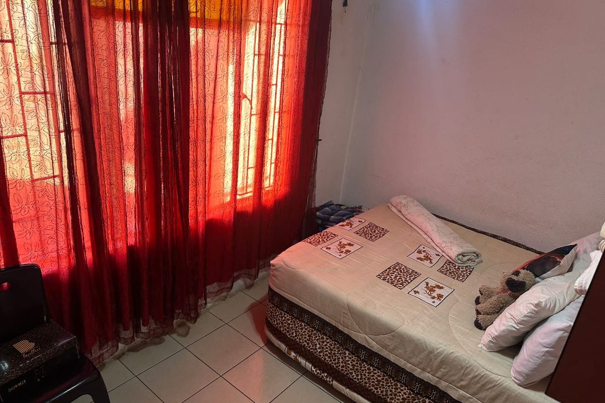 A bedroom featuring tiled flooring and large windows with security bars, currently requiring cosmetic updates to the wall finishes.