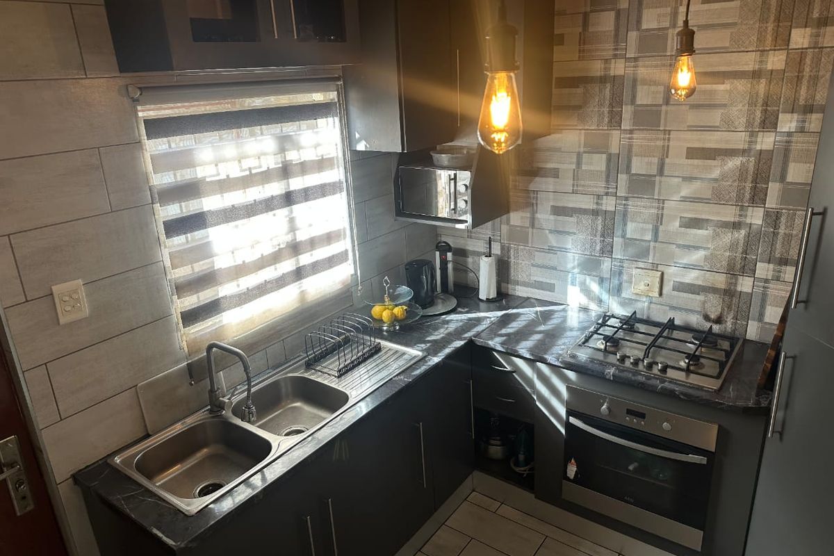 Modern kitchen featuring dark cabinetry, a double bowl stainless steel sink, built-in oven, gas hob, and stylish tiled backsplash.