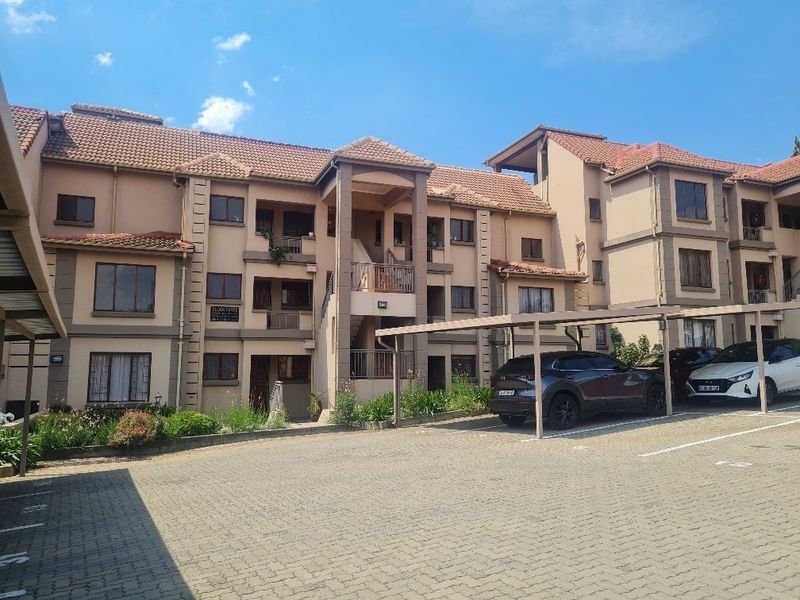 Front elevation of a multi-story apartment complex featuring tiled roofing, private balconies, and a paved parking area with covered carports.