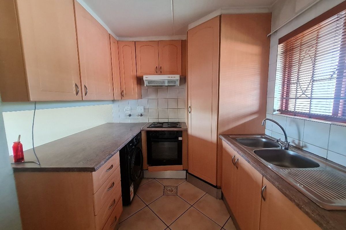 A functional kitchen featuring laminate cabinetry, a double bowl stainless steel sink, built-in oven with hob, and tiled flooring with a tiled backsplash.