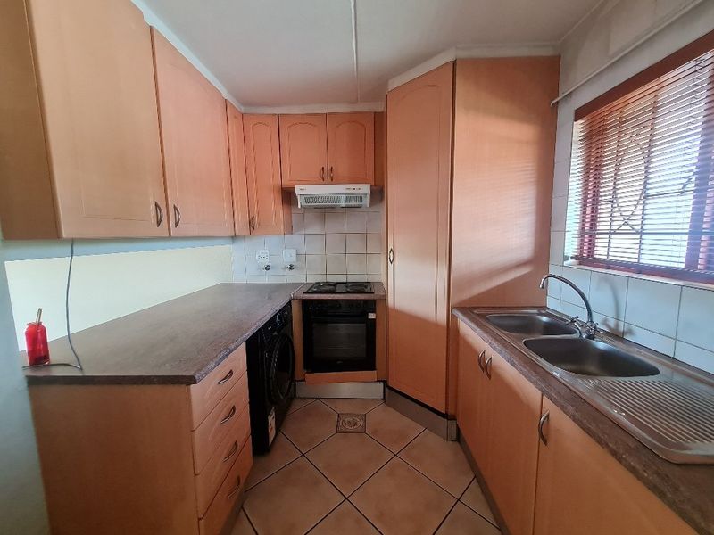 A functional kitchen featuring laminate cabinetry, a double bowl stainless steel sink, built-in oven with hob, and tiled flooring with a tiled backsplash.
