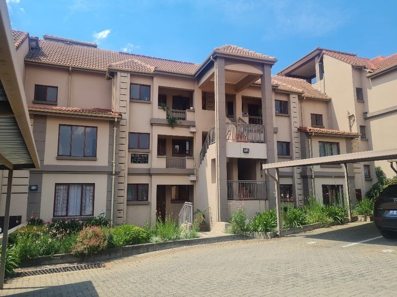 Exterior view of a multi-story apartment complex featuring tiled roofing, private balconies, and a paved driveway with covered parking.