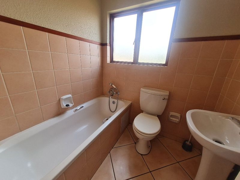 A functional bathroom featuring a bathtub, pedestal basin, and toilet with neutral wall and floor tiling, offering a clean and practical layout.