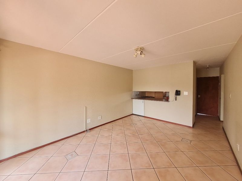 An open-plan living area featuring tiled flooring and a compact kitchen nook with built-in cabinetry and countertops.