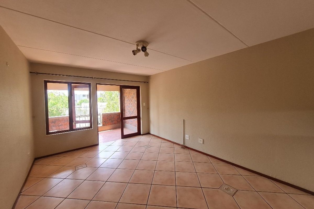 An empty living room featuring ceramic floor tiles, neutral walls, and direct access to an outdoor balcony through a sliding glass door.