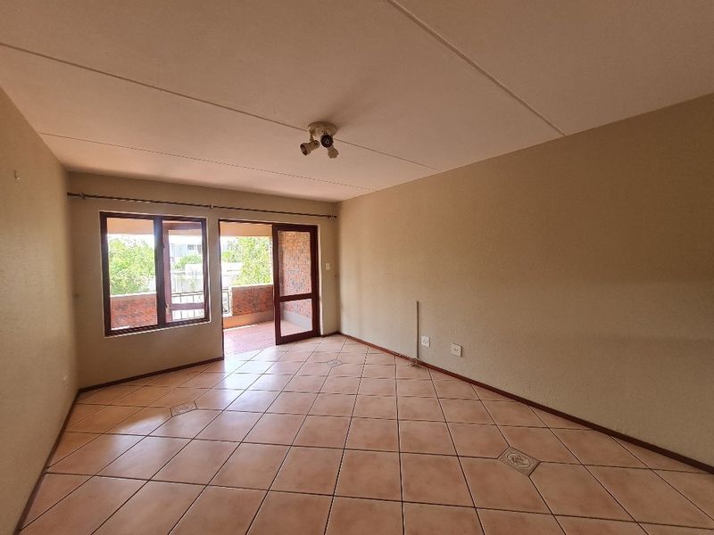 An empty living room featuring ceramic floor tiles, neutral walls, and direct access to an outdoor balcony through a sliding glass door.