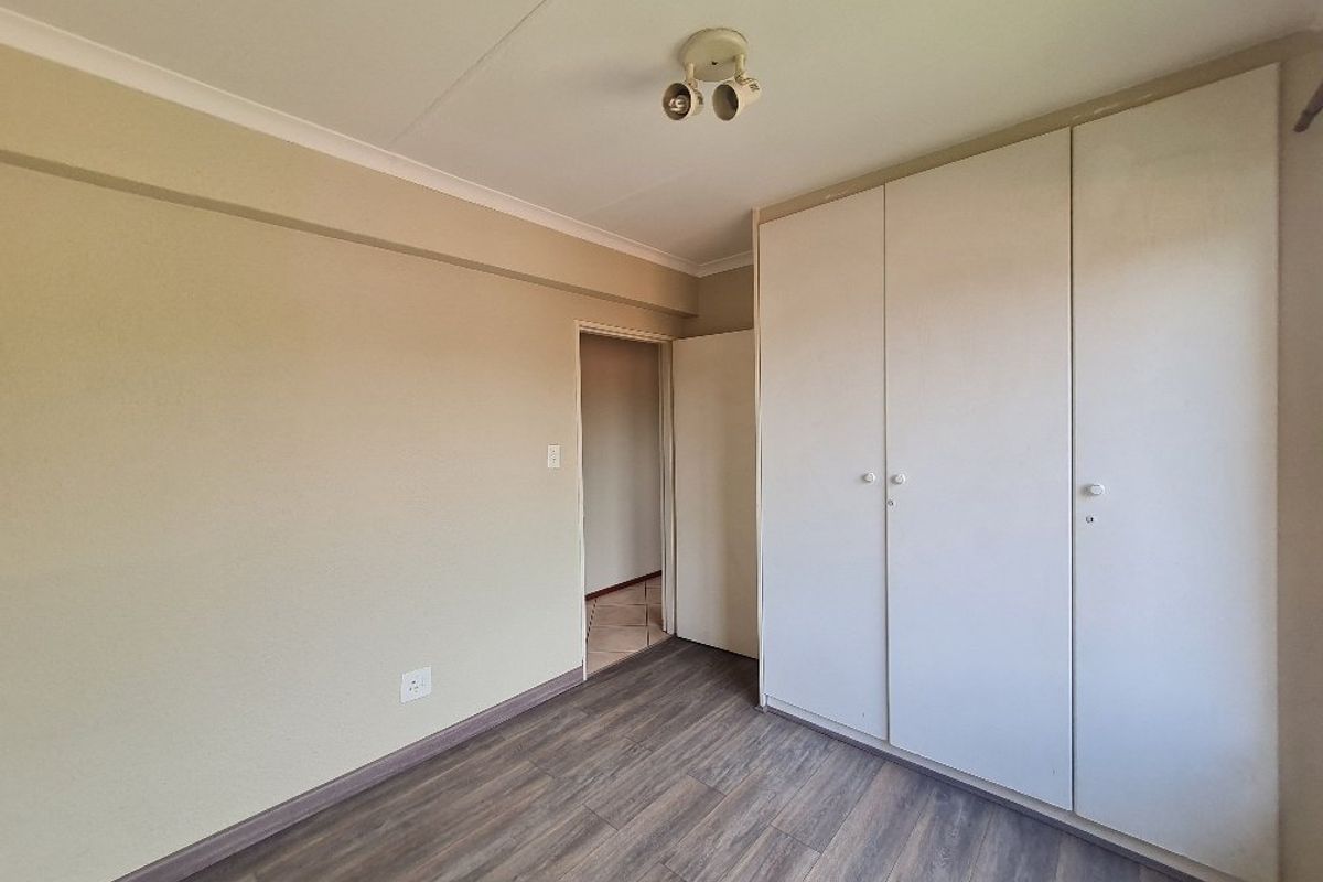 A clean, empty bedroom featuring neutral walls, modern laminate flooring, and ample built-in cupboard storage space.