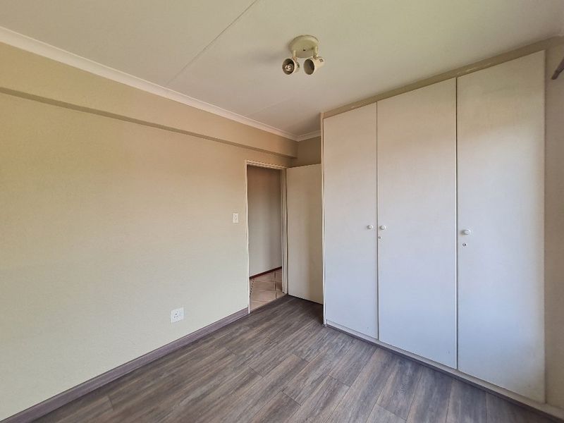 A clean, empty bedroom featuring neutral walls, modern laminate flooring, and ample built-in cupboard storage space.